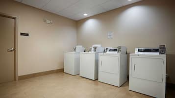 A laundry room with four white front-loading washers and dryers, a storage area, and a guest laundry sign on the wall.