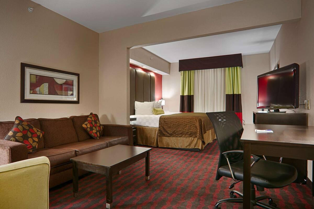 A hotel room with a sofa, a bed, a desk, a chair, and a television.