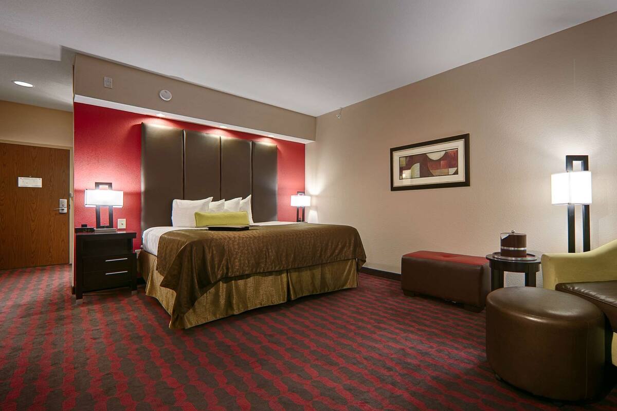 A hotel room with a large bed, a desk, a chair, and a small table with a lamp.