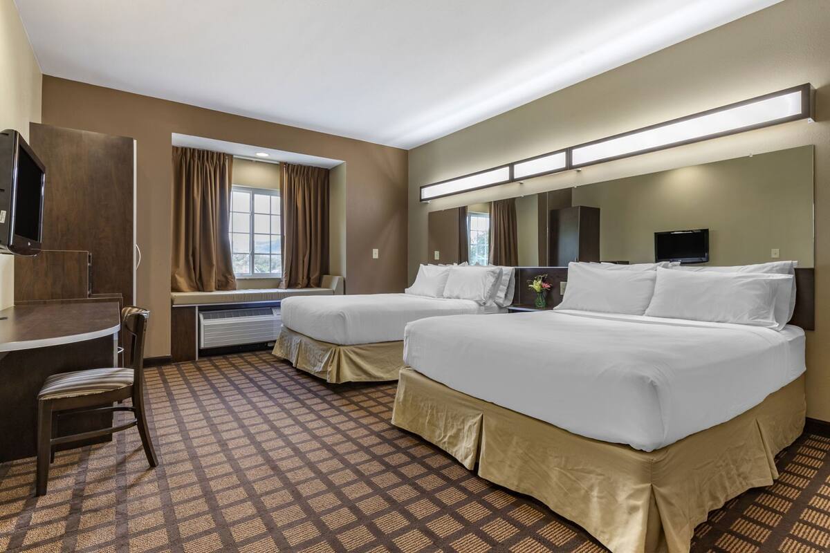 A hotel room with two beds, a desk, a chair, a TV, and a window with curtains.