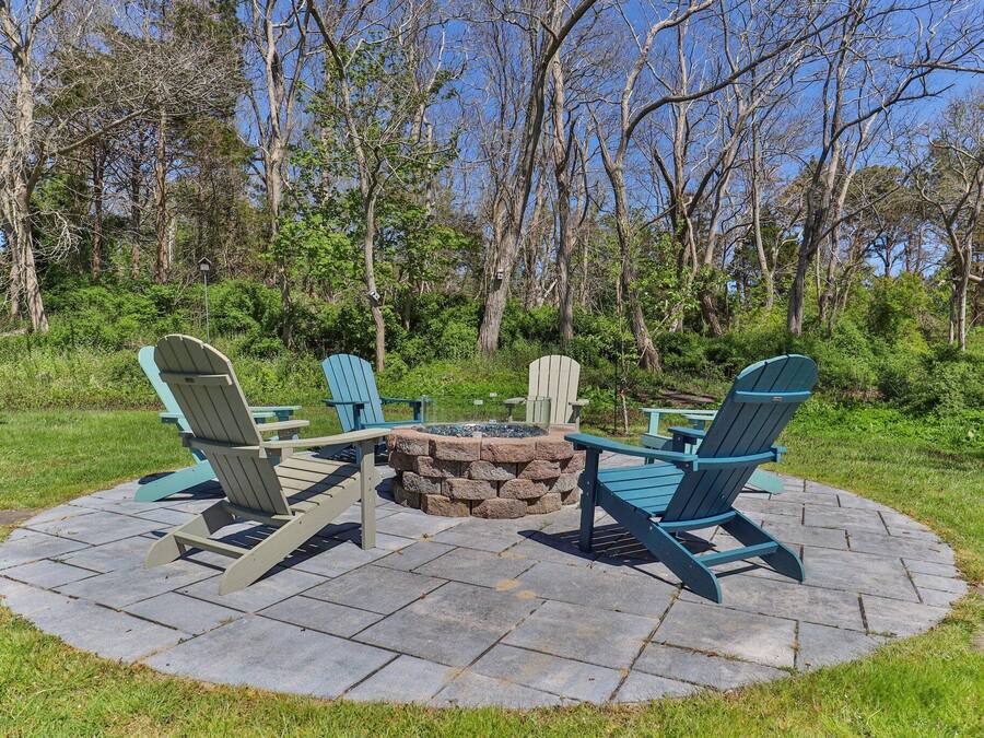 A circular outdoor seating area with Adirondack chairs and a stone fire pit.
