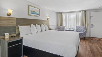 Ein Hotelzimmer mit einem großen Bett, zwei Sesseln, einem kleinen Tisch und einem Bild an der Wand.
