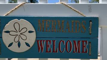 A wooden sign with the words "Mermaids Welcome" and a decorative flower emblem.