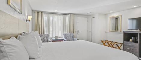 A hotel room with a large bed, a desk with a chair, a TV, and a wardrobe.