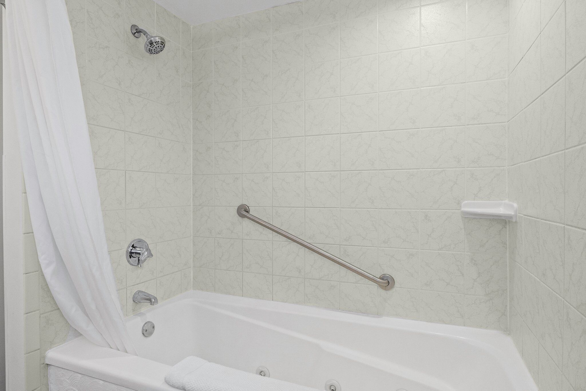 Un baño con bañera, ducha, barra de apoyo y cortina blanca.