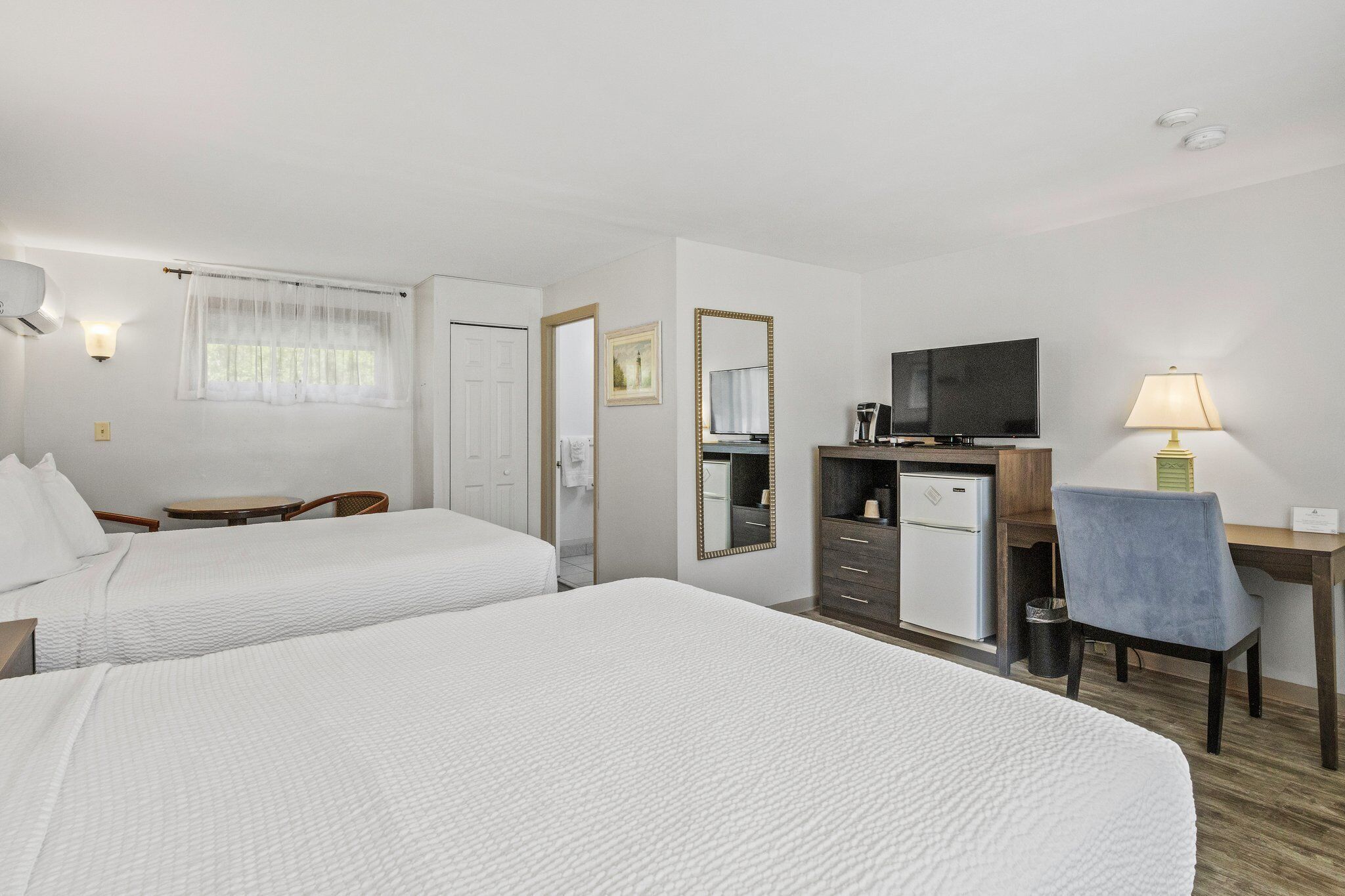 Quarto de hotel com duas camas, uma escrivaninha, uma televisão e uma cadeira.