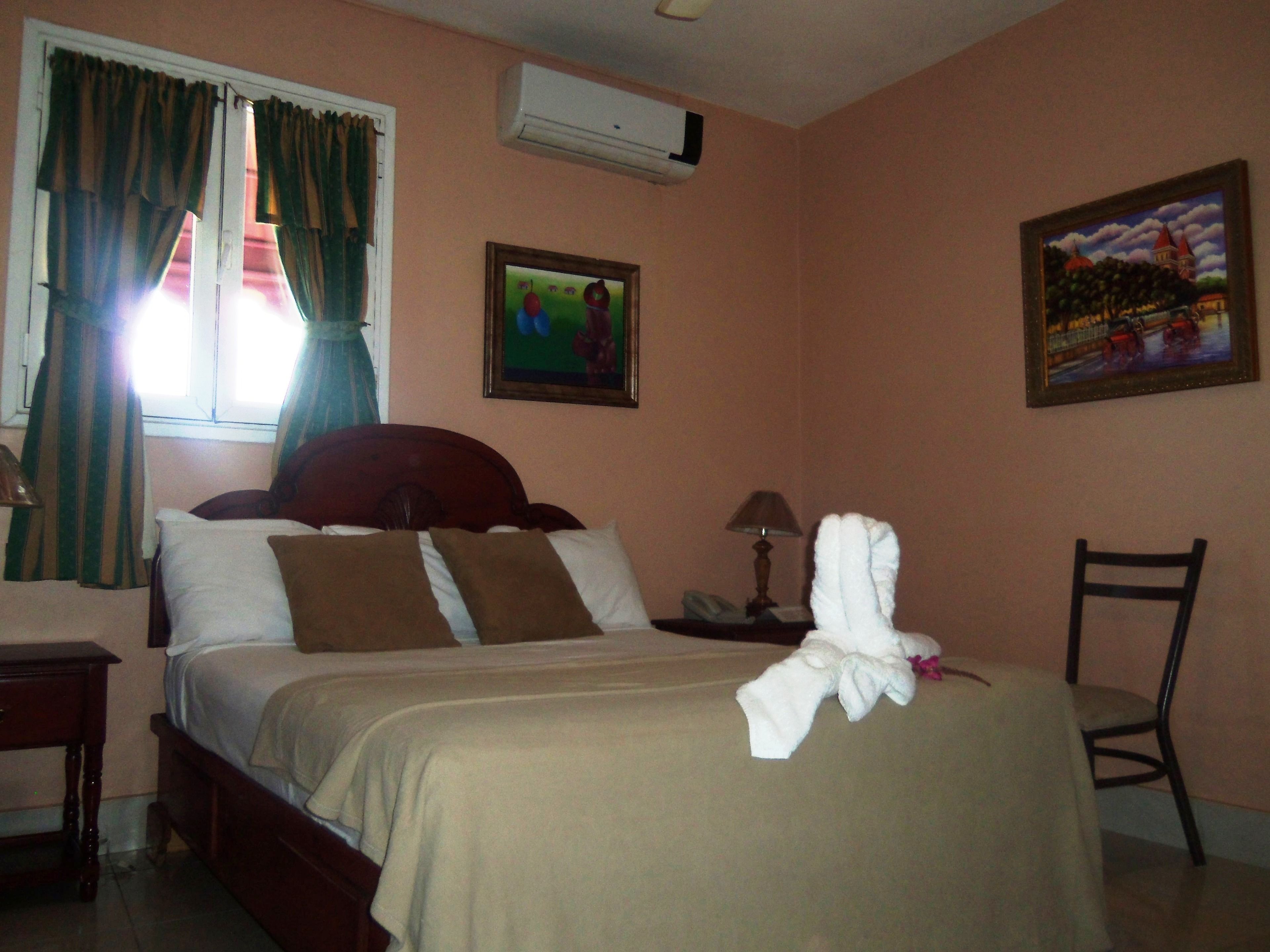 A hotel room with a bed, a nightstand, a chair, a lamp, and two paintings on the wall.