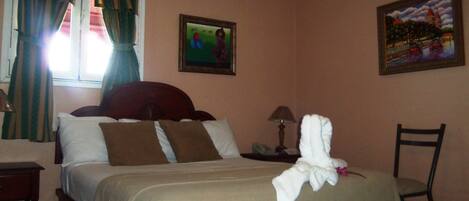 A hotel room with a bed, a nightstand, a chair, a lamp, and two paintings on the wall.