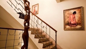 A staircase with a wooden handrail and a metal railing, a framed painting on the wall, and a decorative wall piece. - Hotel Discovery (Santo Domingo)