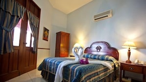 A hotel room with a bed, two bedside lamps, a wooden wardrobe, and a wall-mounted air conditioner. - Hotel Discovery (Santo Domingo)