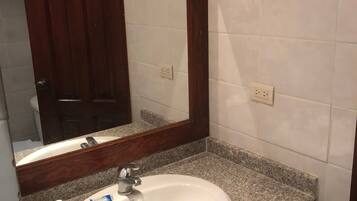 Un baño con lavamanos blanco, encimera de granito y mueble de tocador de madera.