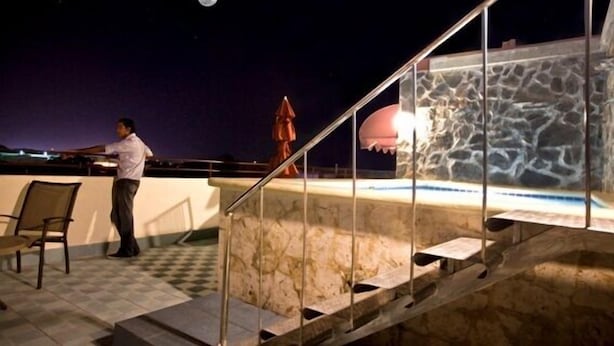 A rooftop bar with a stone wall, a pool, and a chair. - Hotel Discovery (Santo Domingo)