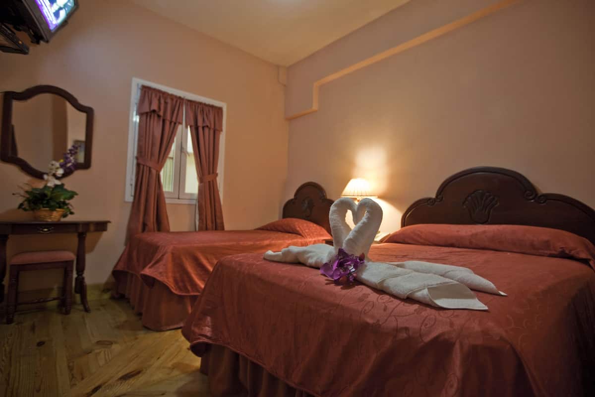 A hotel room with two beds, a desk, a chair, a mirror, and a window with curtains.