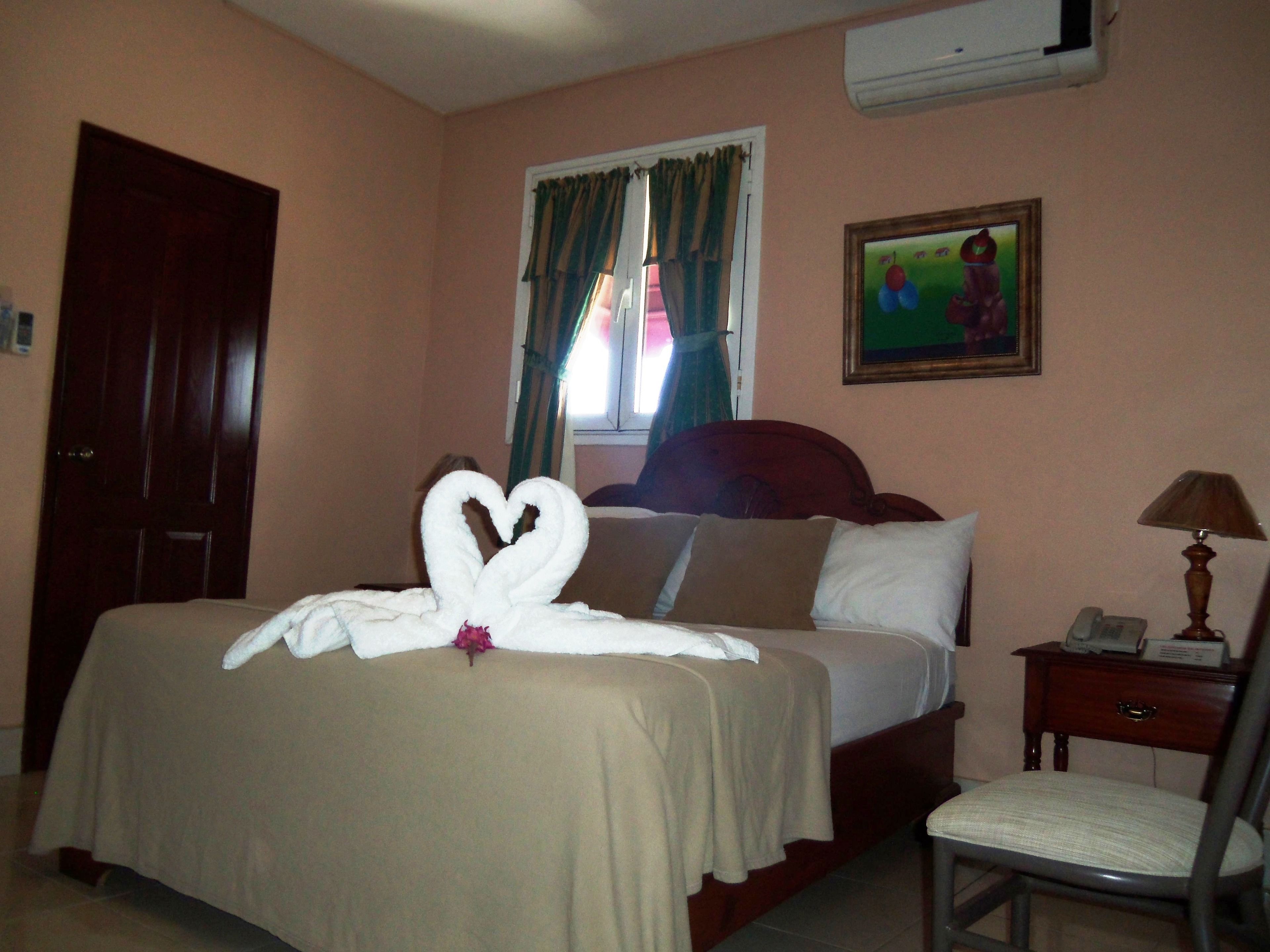 Habitación de hotel con cama, una silla, mesita de noche, un cuadro en la pared y una puerta.