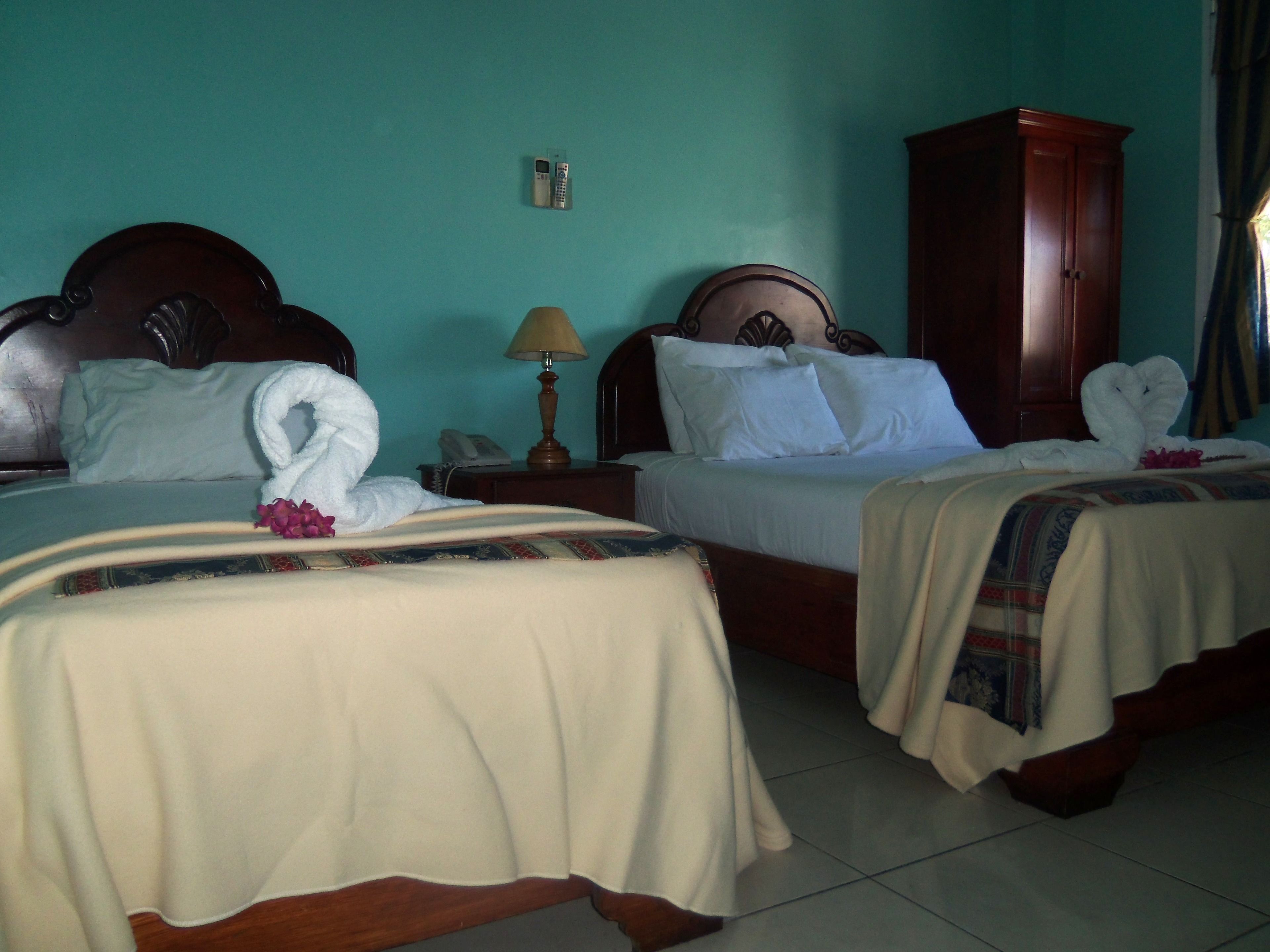 A hotel room with two beds, a wooden wardrobe, a bedside table with a lamp, and a telephone.