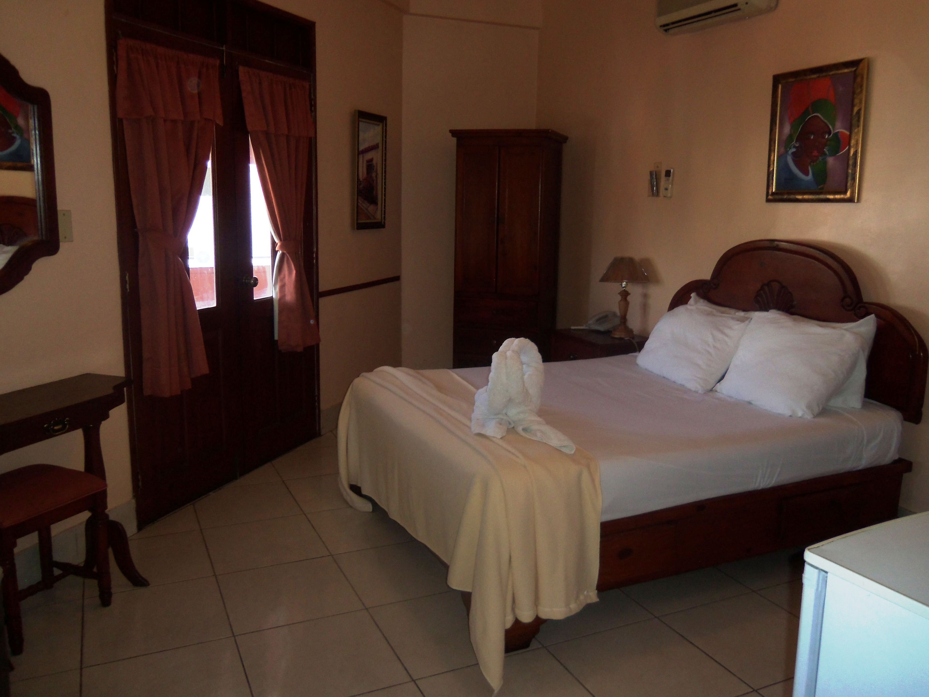 A hotel room with a bed, a desk, a chair, a wardrobe, and a painting on the wall.