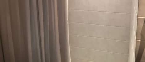 A shower area with a white shower curtain, tiled walls, and a metal shower tray.