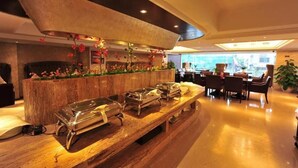 Un'area buffet con diverse postazioni di servizio, un bancone in legno e una zona salotto con tavoli e sedie.