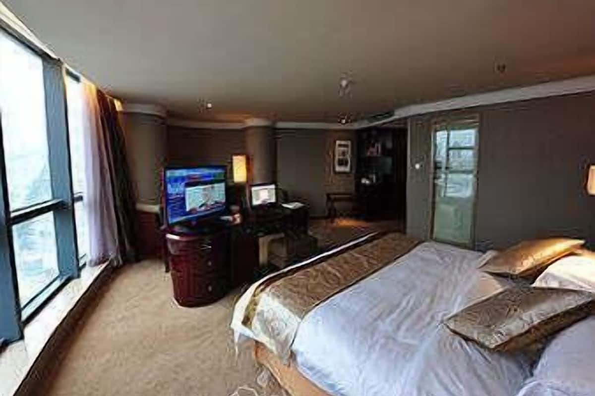Habitación de hotel con una cama grande, un escritorio con computadora, televisor y ventana que ofrece vistas al exterior.