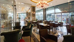 Un restaurant spacieux avec de hauts plafonds, des lustres et de grandes fenêtres offrant une vue sur l’extérieur.