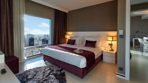 Une chambre d’hôtel moderne avec un grand lit, des lampes de chevet, une vue sur la ville et un petit bureau.