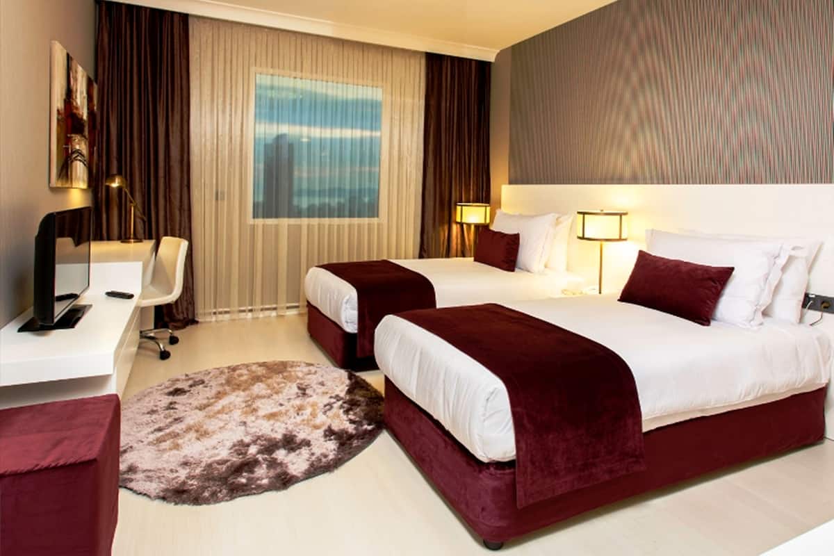 A hotel room with two beds, a desk, a chair, and a large window with curtains.