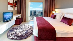 Une chambre d’hôtel moderne dotée d’un grand lit, d’un téléviseur à écran plat, d’une vue sur la ville et d’un tapis confortable.