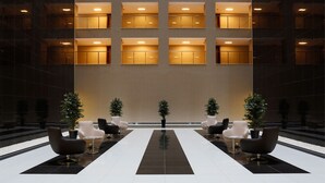 Un hall d’entrée moderne doté d’un sol central réfléchissant, d’un agencement symétrique des sièges et d’un grand mur orné de fenêtres régulièrement espacées.