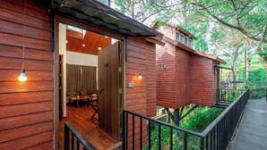 Een houten chalet met een balkon, een deur naar de binnenruimte en uitzicht op begroeiing.