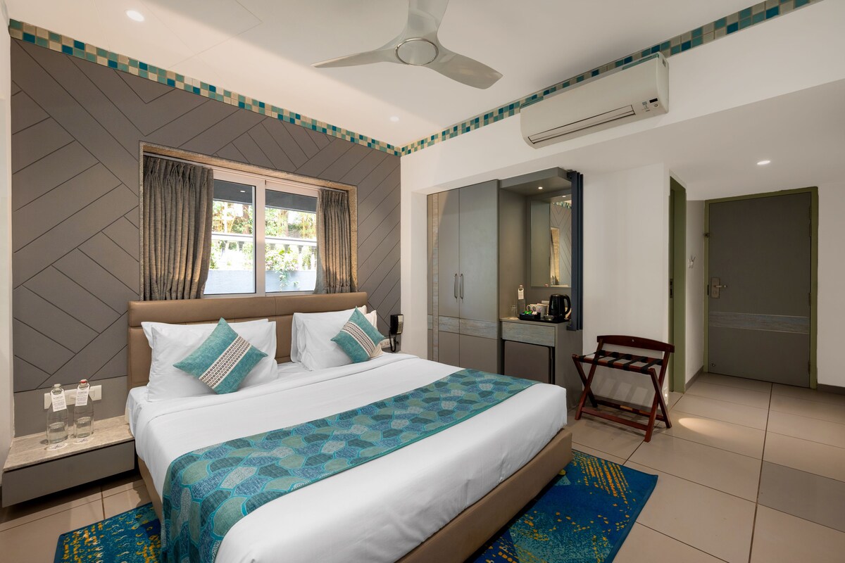 Habitación de hotel con cama, ventilador de techo, aire acondicionado, escritorio, espejo y puerta.