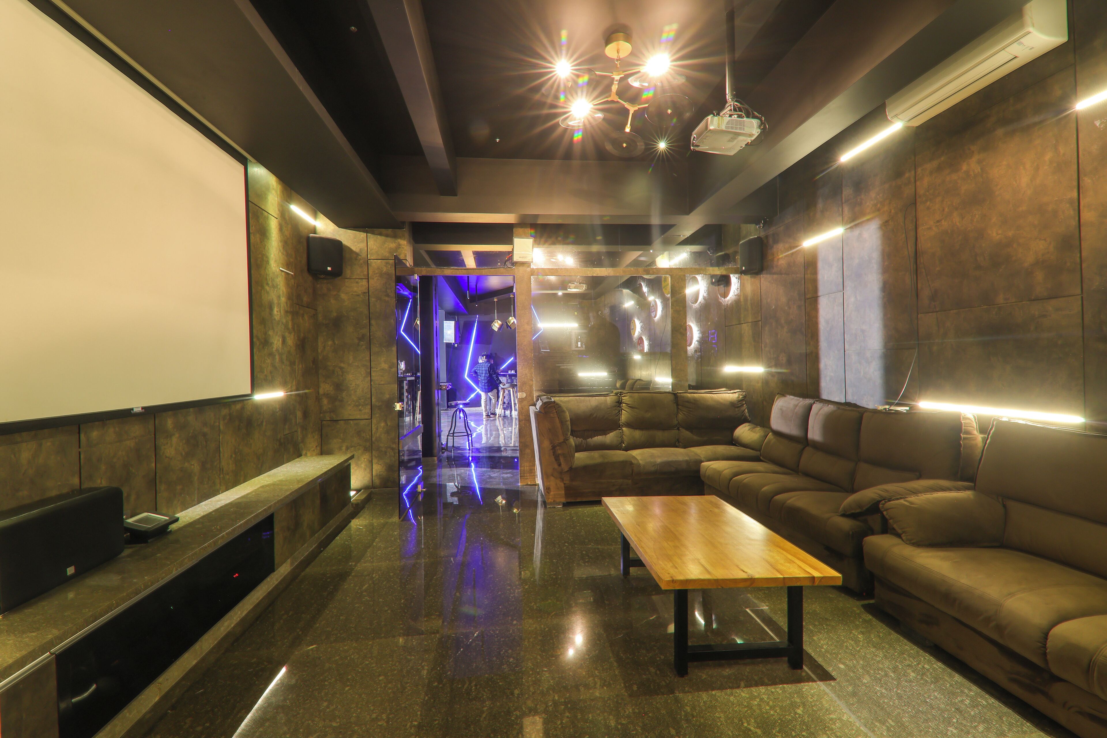 A modern lounge with a large screen, leather couches, and ambient lighting.