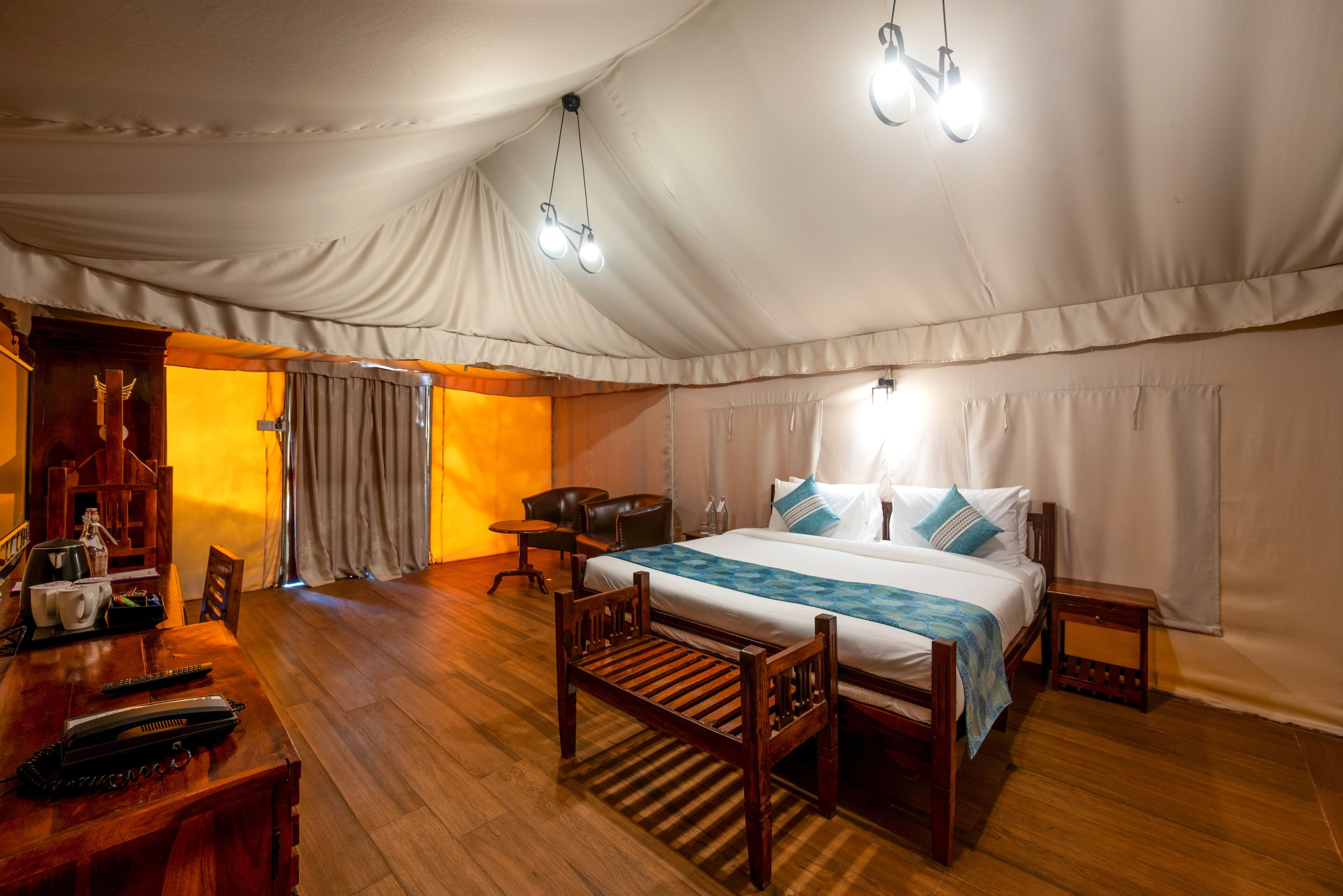 A tented room with a bed, wooden furniture, and a table with a kettle and remote controls.
