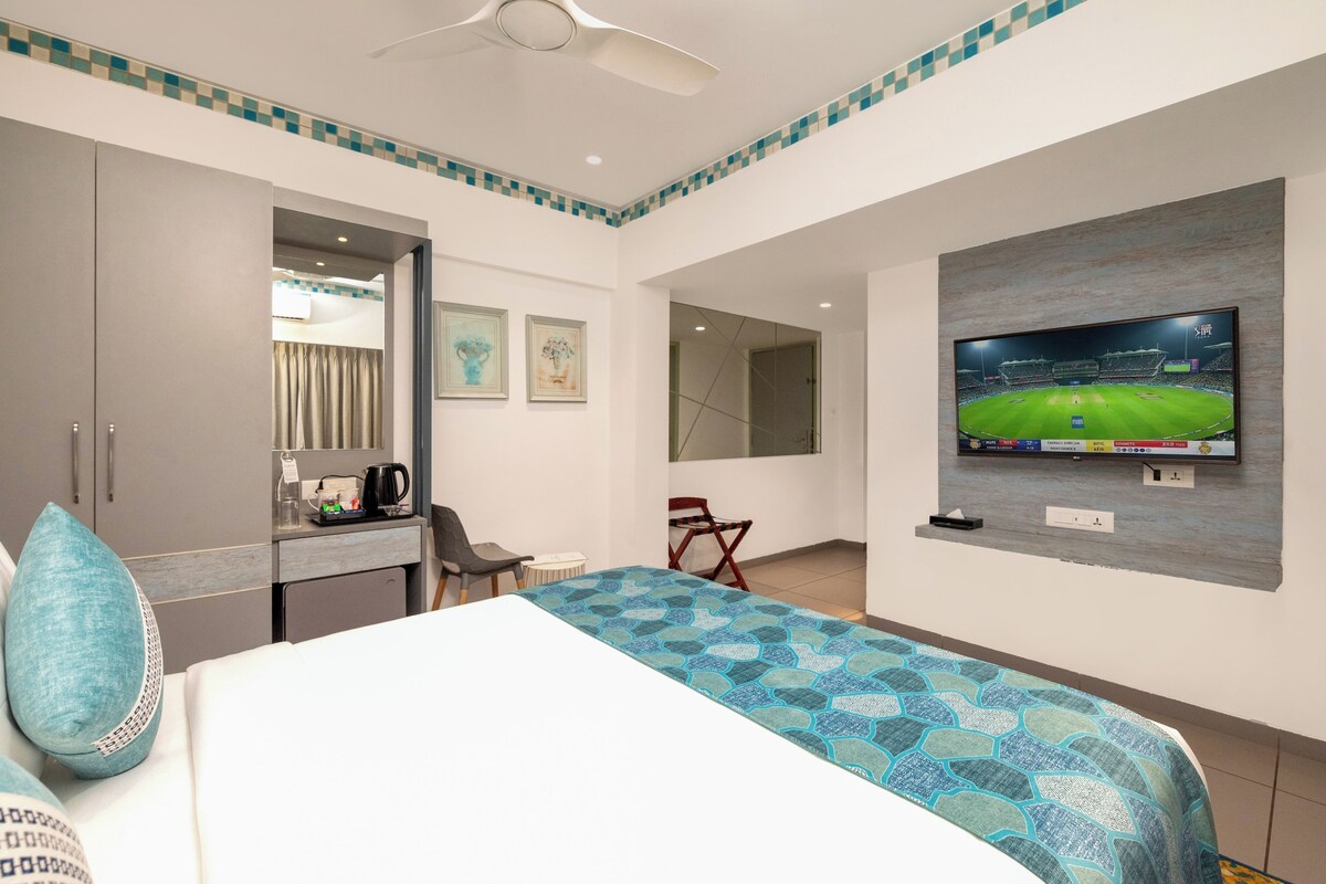 Una habitación de hotel con cama, escritorio, silla, televisor y ventilador de techo.