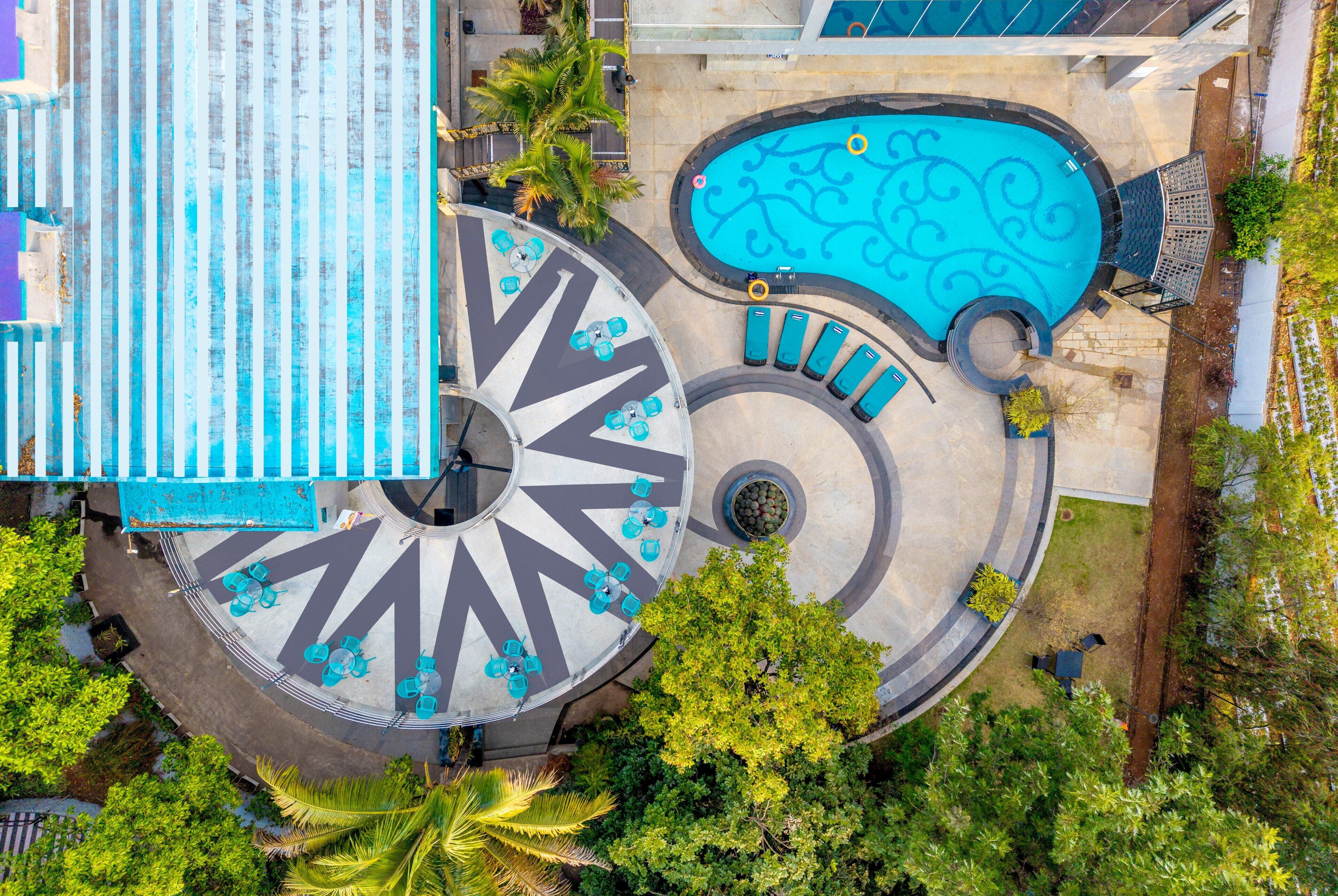 An aerial view of a resort with a swimming pool, sun loungers, and a circular seating area.