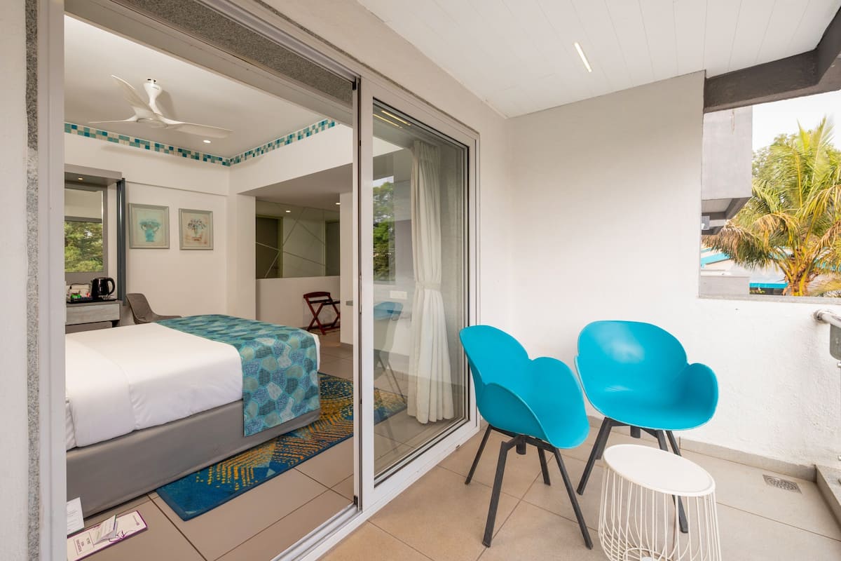 Moderni hotellihuone, jossa on sänky, työpöytä, tuoli ja parveke, jossa on myös tuoleja.