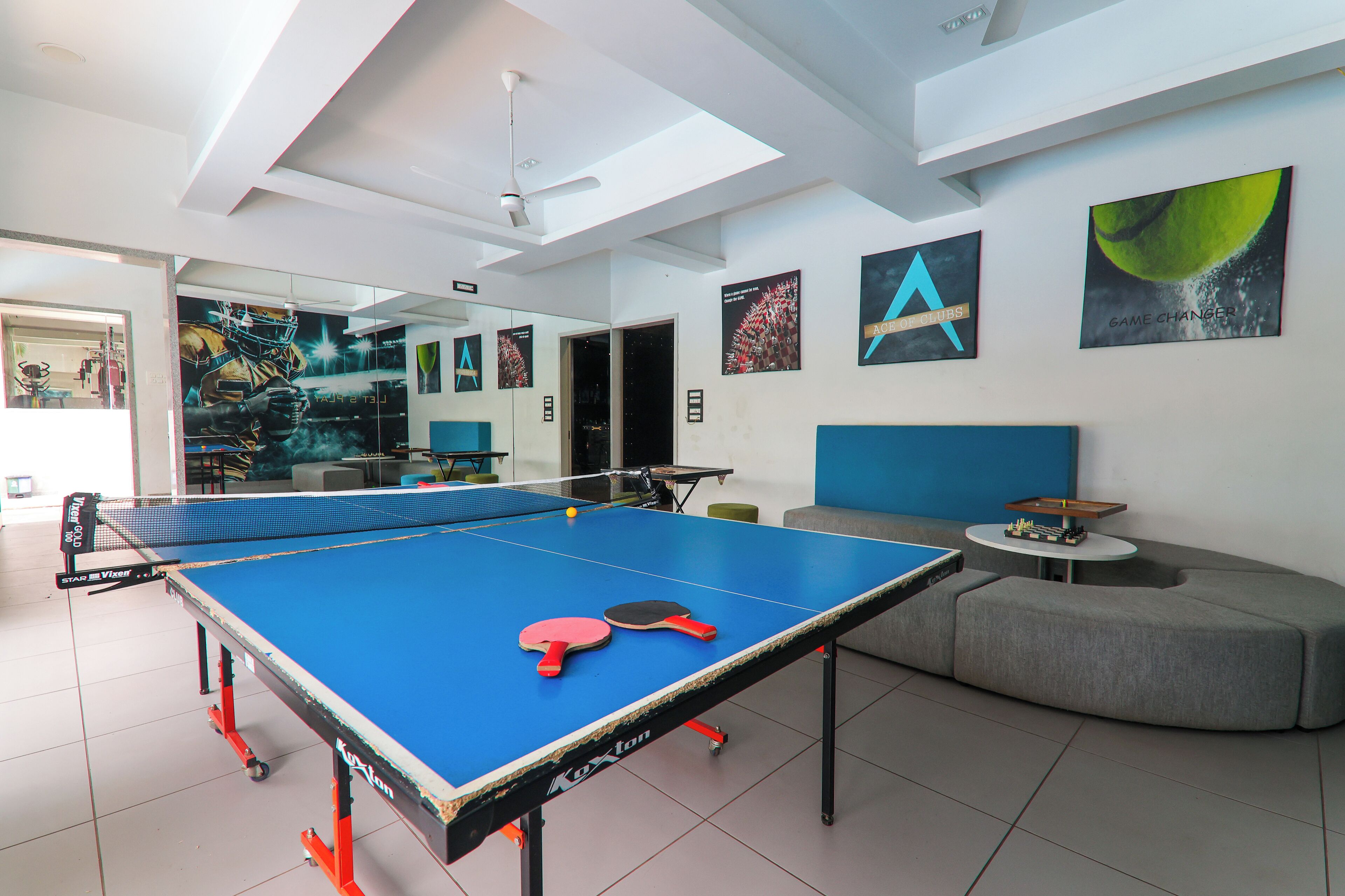 Una mesa de ping pong con dos paletas, un sofá y una mesita con un juego de ajedrez.