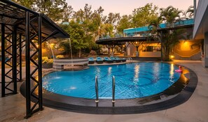 A swimming pool with a circular design, a covered seating area, and a staircase leading to an upper level. - Orchid Hotel Panchgani (Mahabaleshwar)