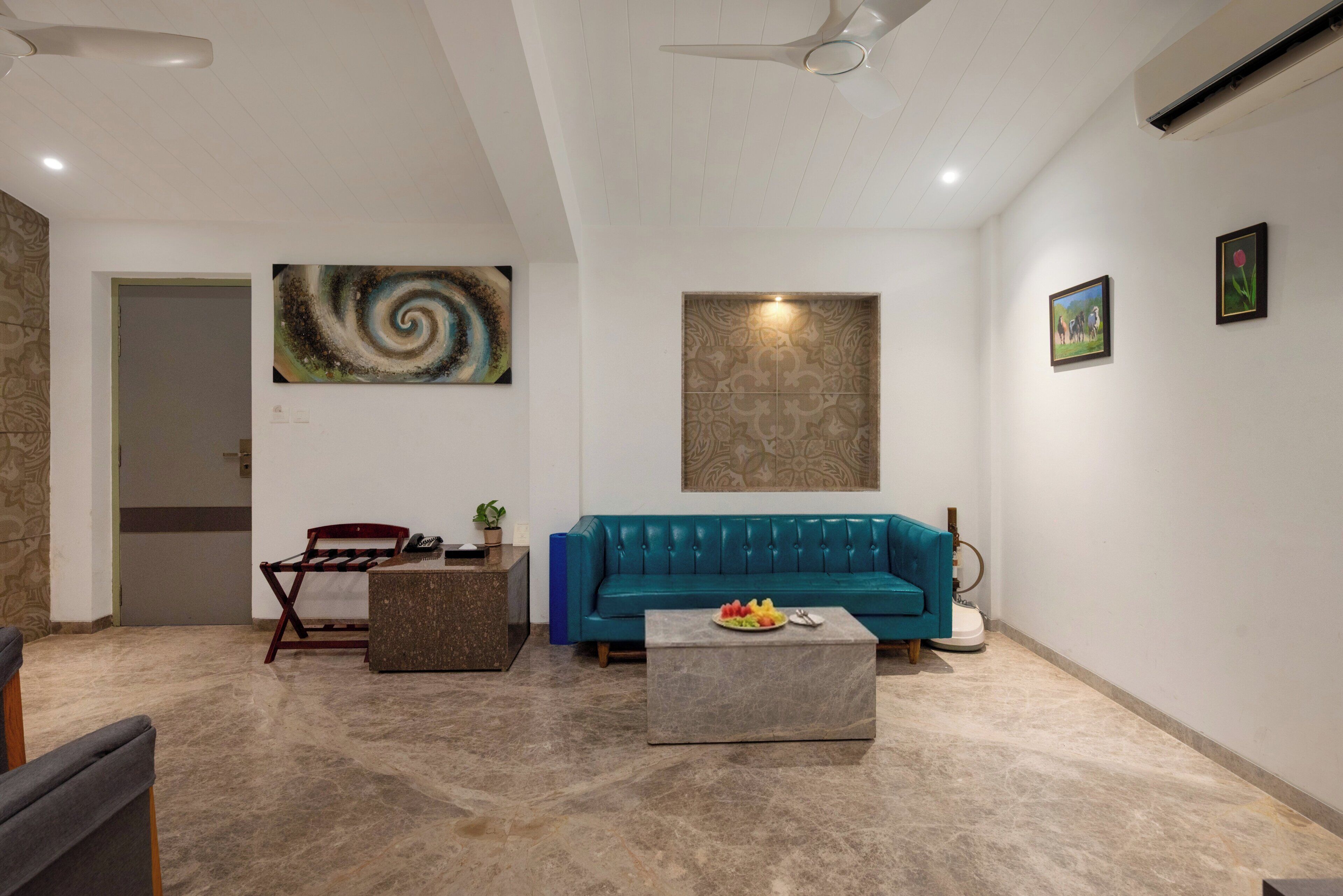 Una sala de estar moderna con un sofá color turquesa, una mesa de centro con fruta, una pared con diseño y un ventilador de techo.