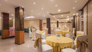 Un salón de banquetes con mesas redondas y sillas, cada una con mantel adornado con un lazo dorado.
