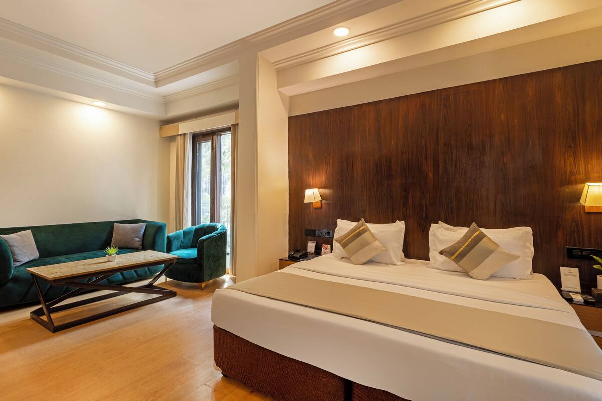 Une chambre d’hôtel avec un grand lit, un canapé vert, une tête de lit en bois et une petite table.