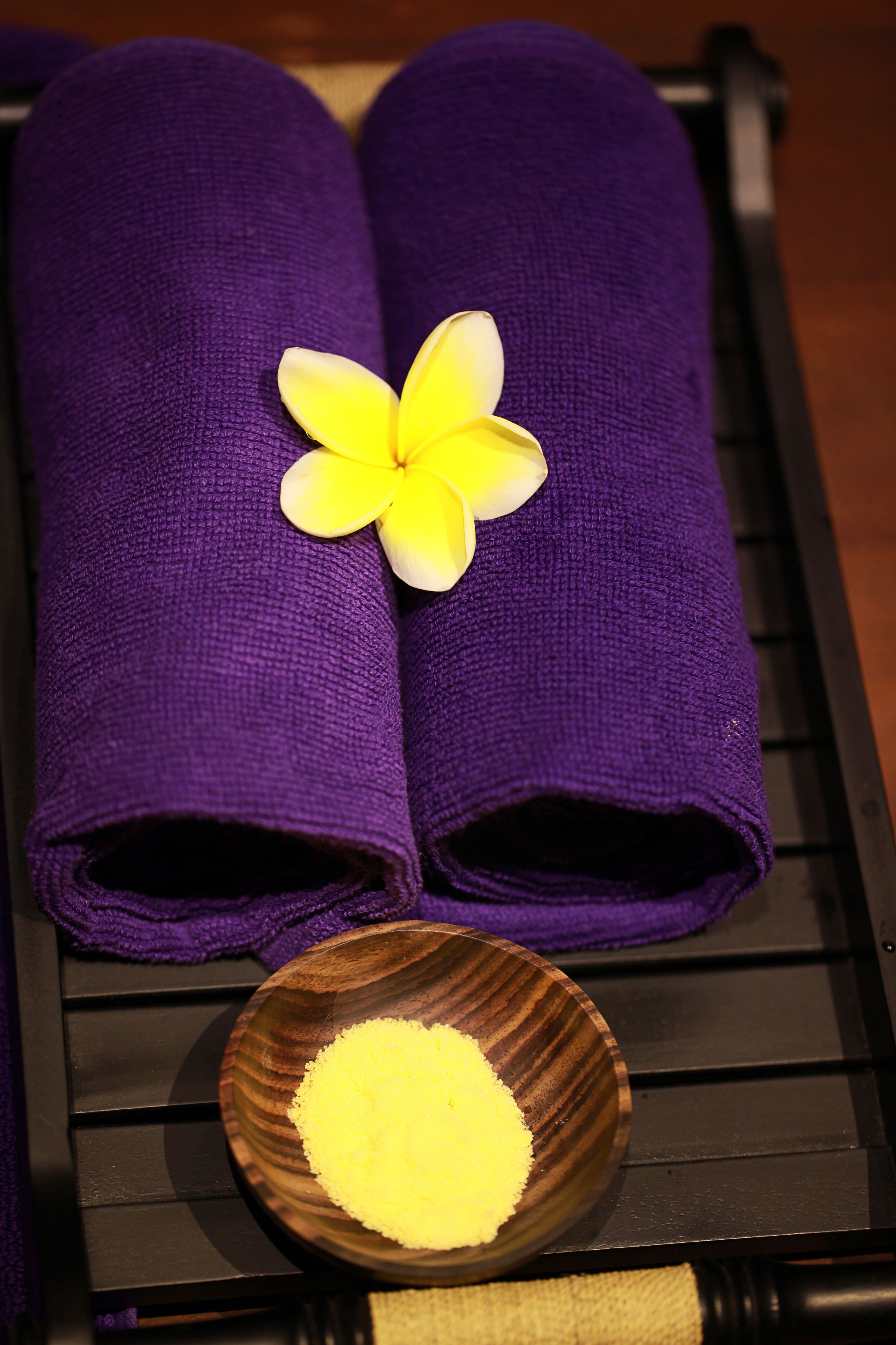 Two rolled purple towels with a yellow flower on top, placed on a black surface.