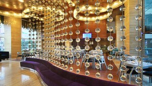 A modern interior with a curved purple seating area, wooden ceiling with hanging spherical mirrors, and a dining area with tables and chairs. - Grand Mega Resort & Spa Bali (Kuta)