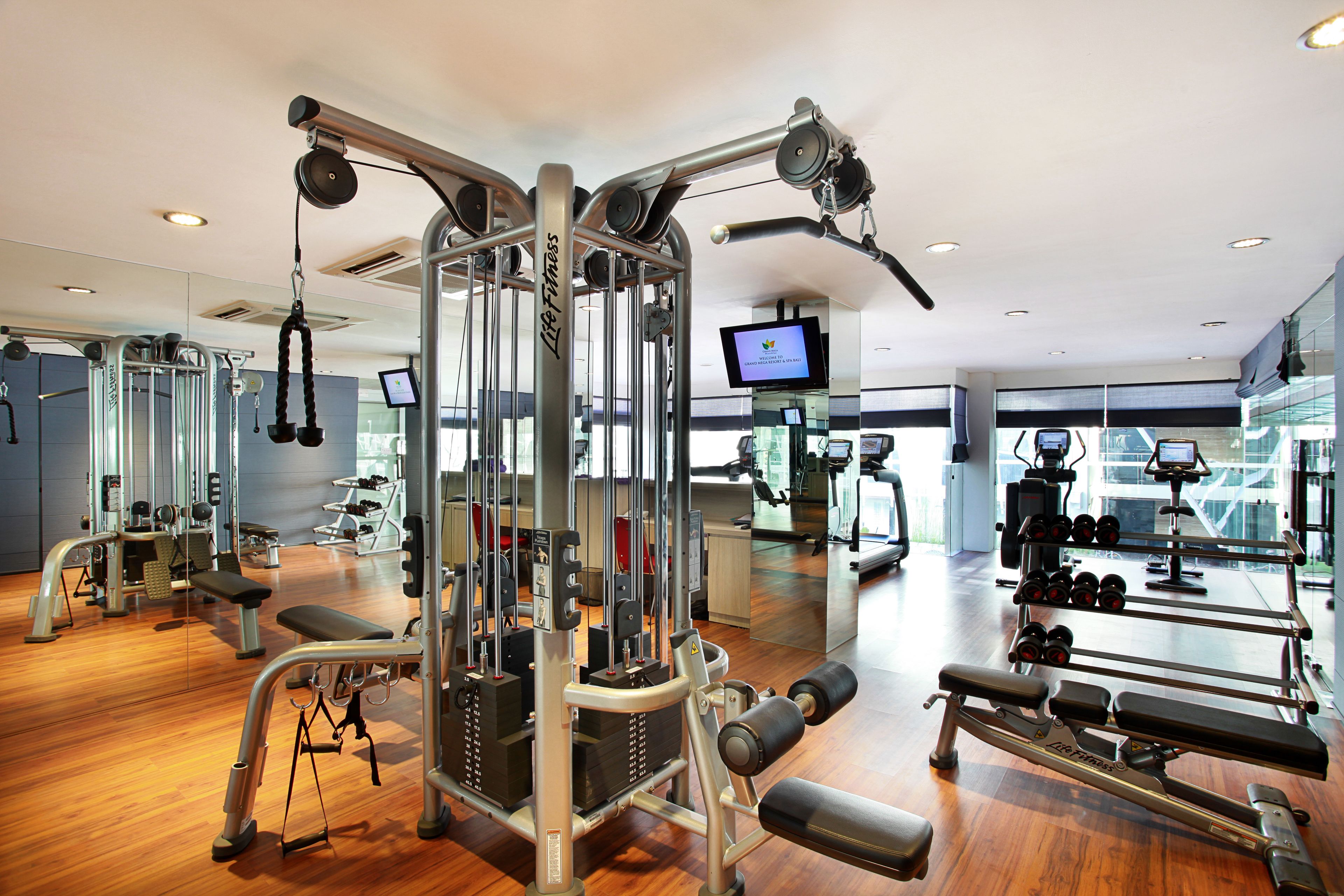 A gym with various exercise equipment, a digital screen, and a large mirror.