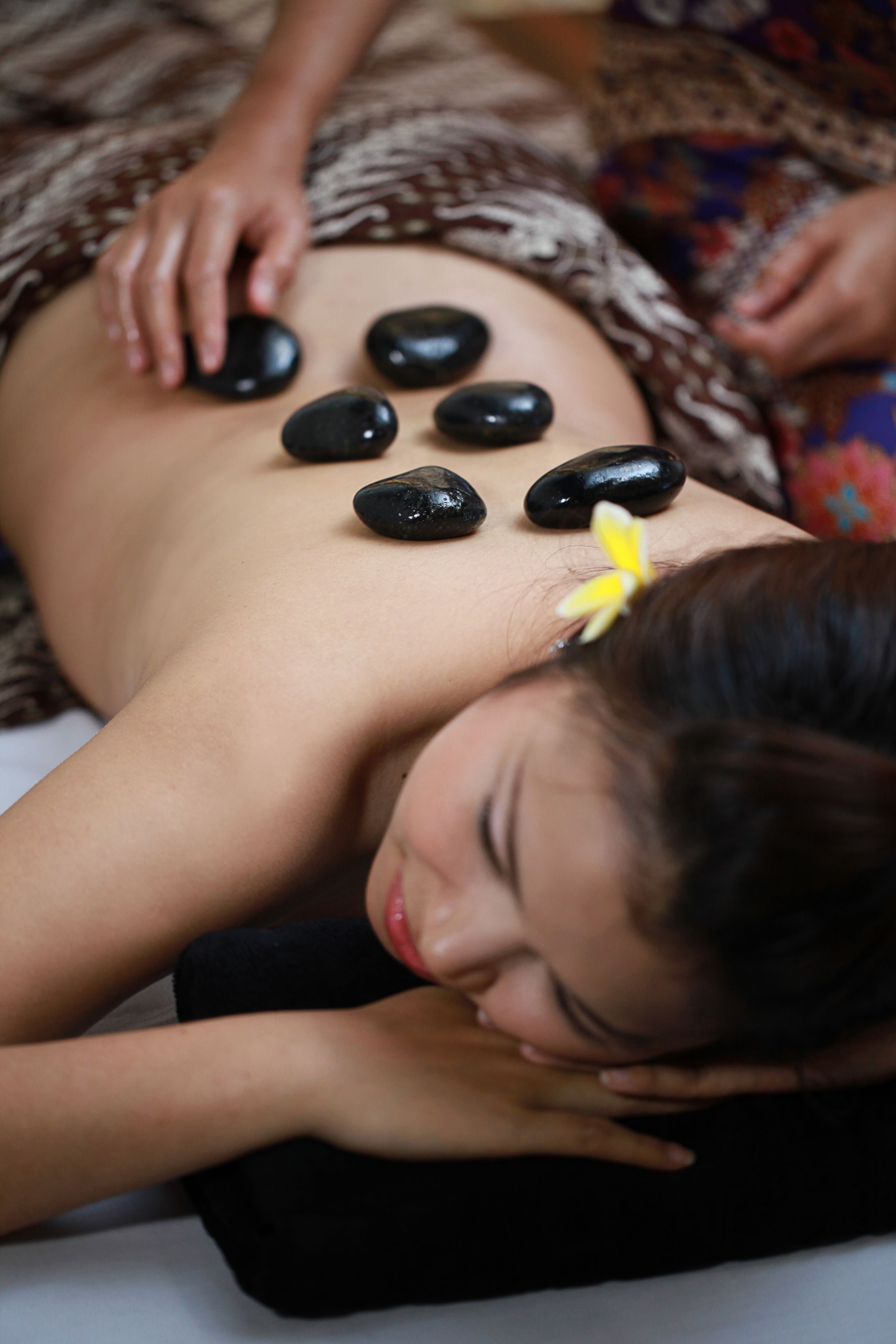 A person receiving a back massage with black stones placed on their back.