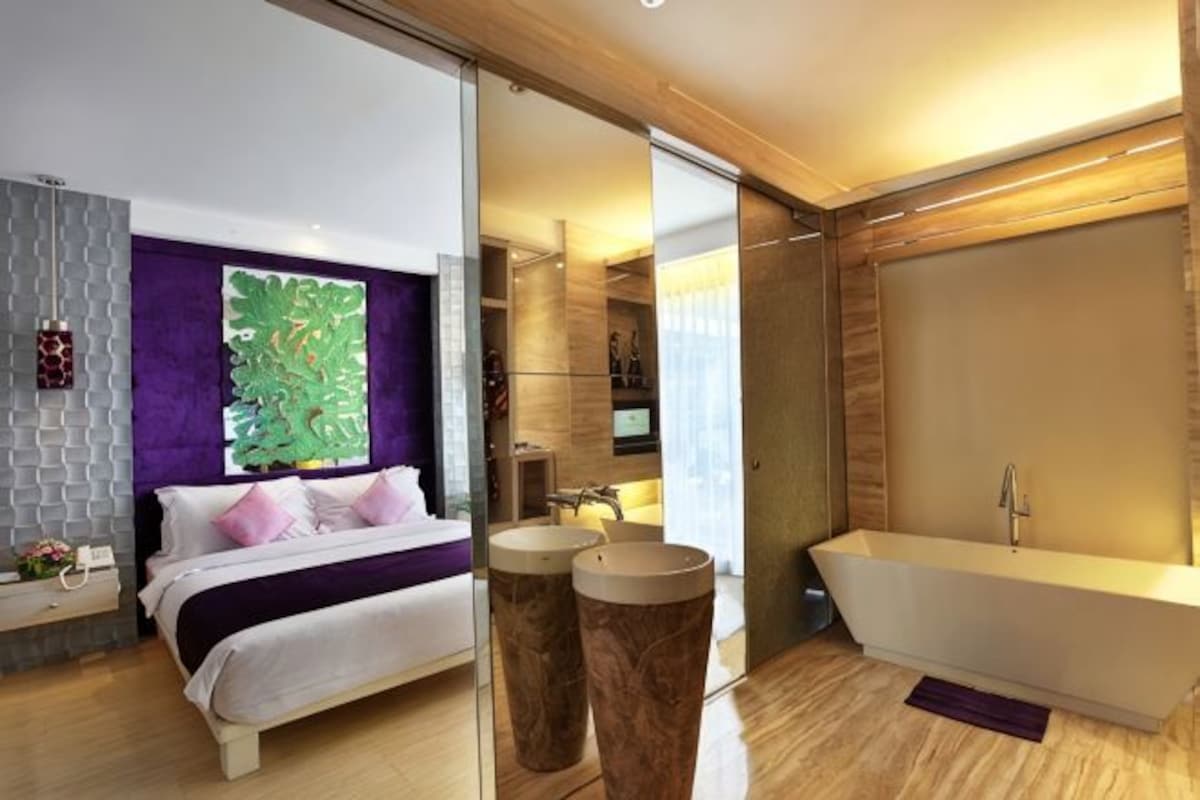 Un dormitorio moderno con cama, un ventanal amplio, un baño con bañera y un espejo.