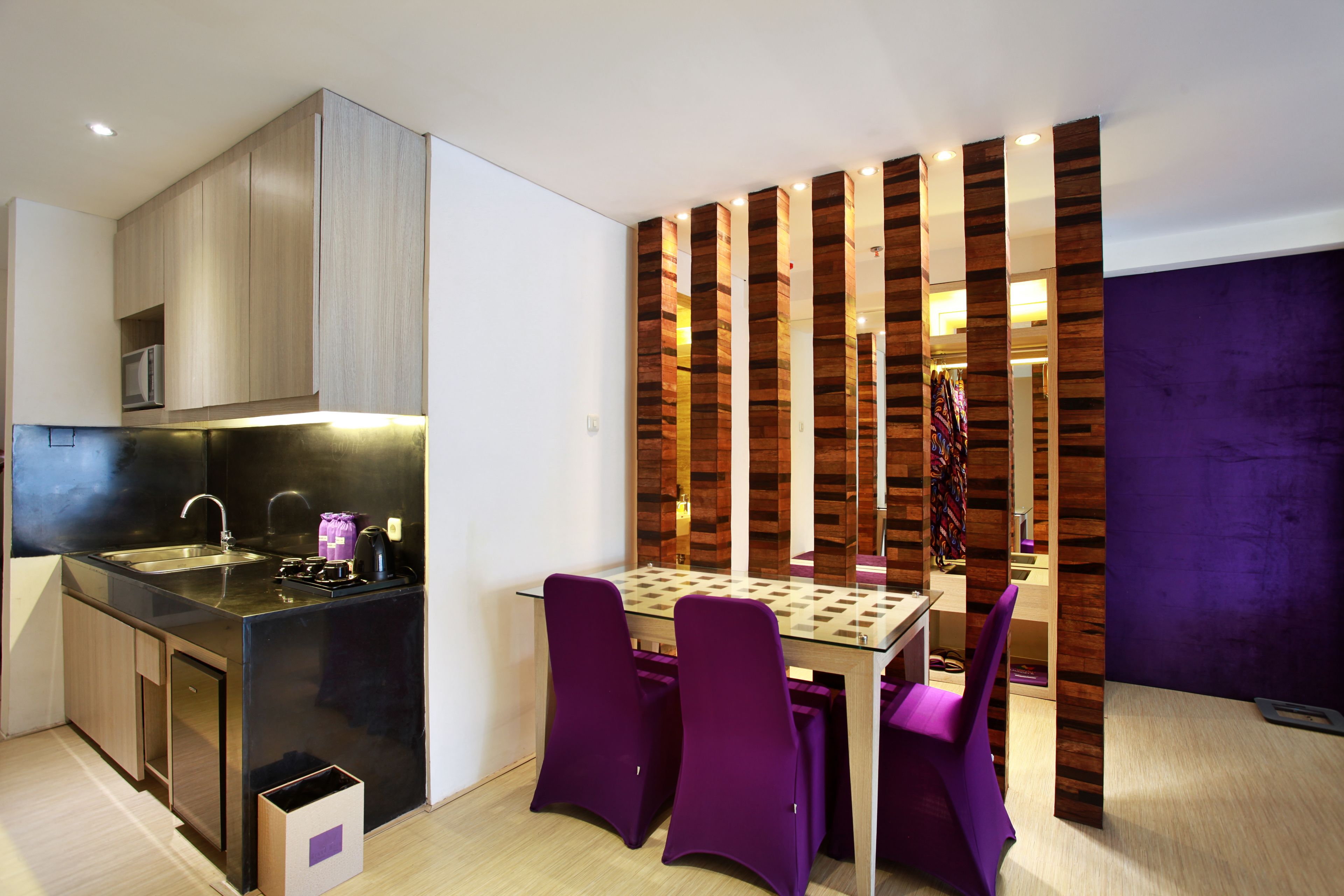 A modern kitchen with a black countertop, stainless steel sink, and purple chairs.