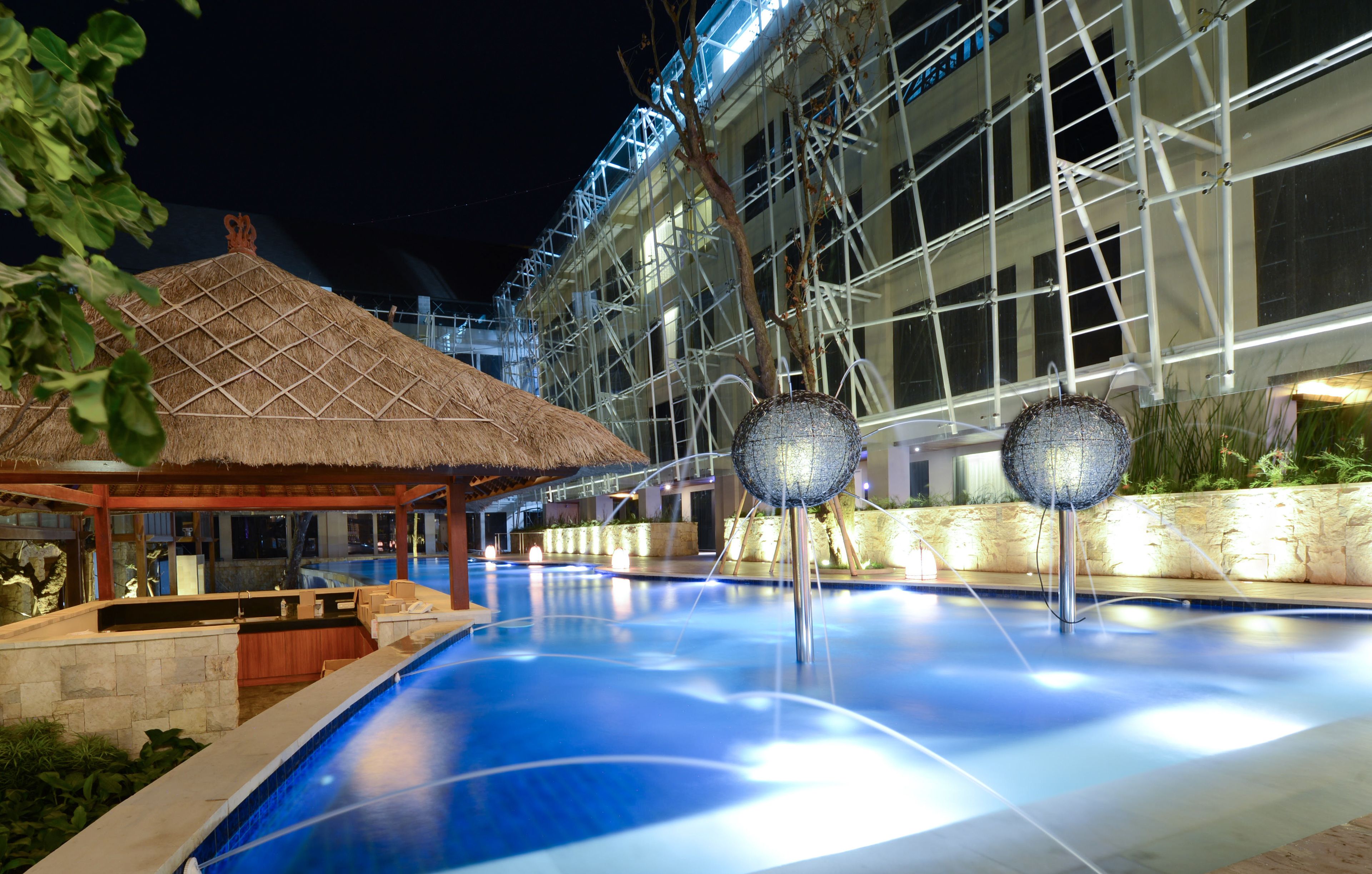 A swimming pool with a thatched-roof structure and two spherical light fixtures.