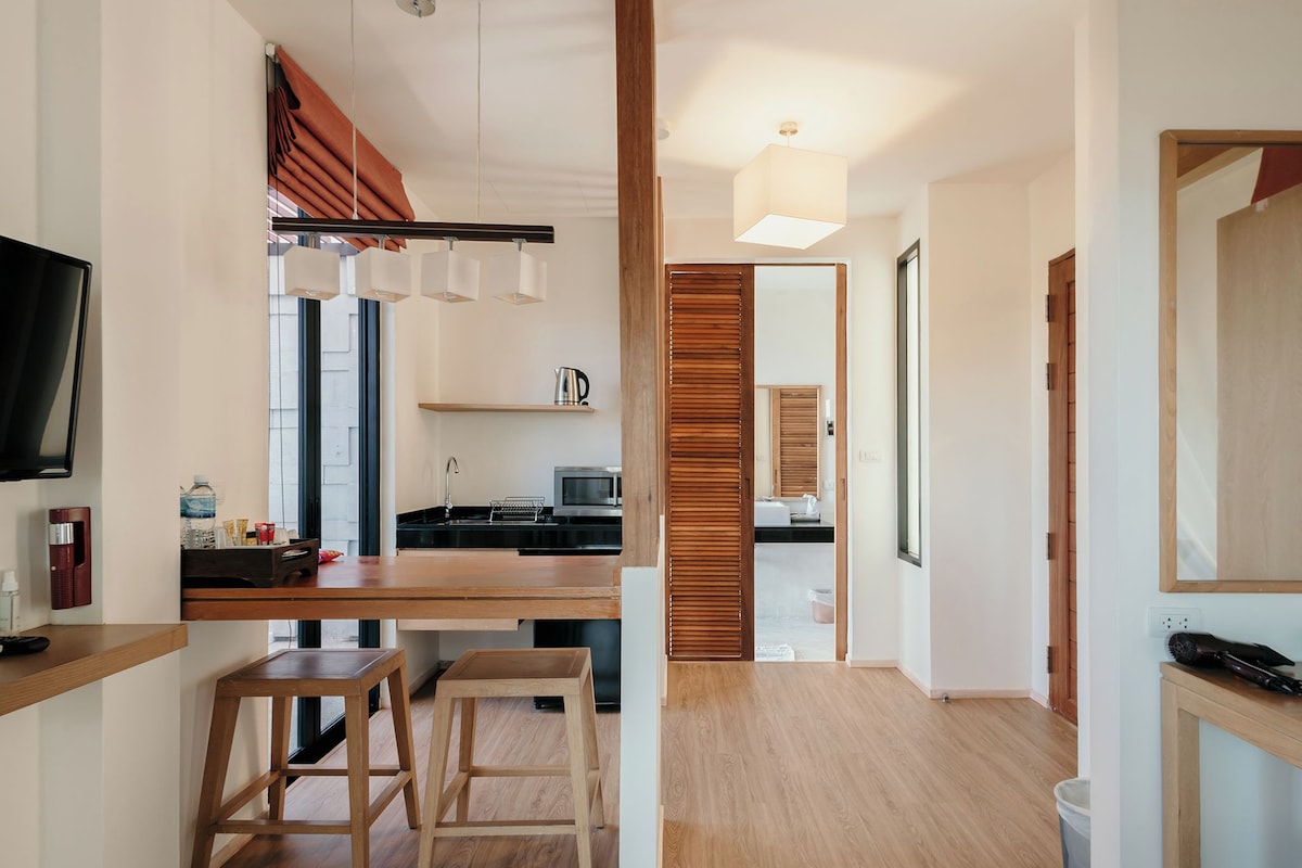 Une cuisine moderne avec des plans de travail en bois, un coin repas avec des tabourets et une vue sur une chambre.
