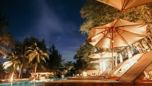A poolside area with lounge chairs and umbrellas, surrounded by palm trees and a night sky. - The Mangrove Panwa Phuket Resort (Wichit)