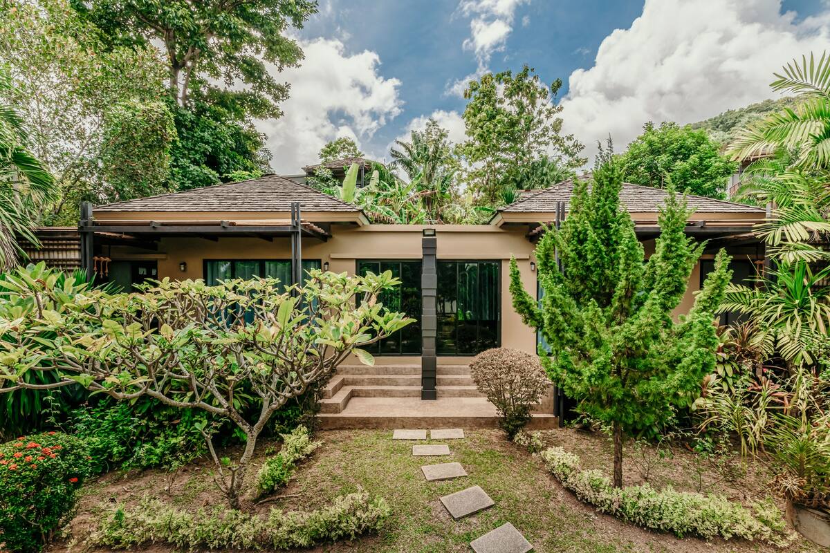 Una casa con jardín y una escalera que conduce a la entrada, bajo un cielo despejado.